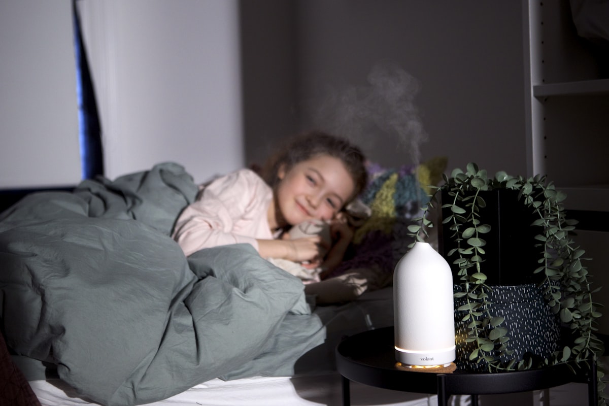 Girl smiling while resting on a bed with a white volant diffuser on her bedside table. related to The Ultimate Guide to Choosing a Bed Bath & Beyond Humidifier for Your Home