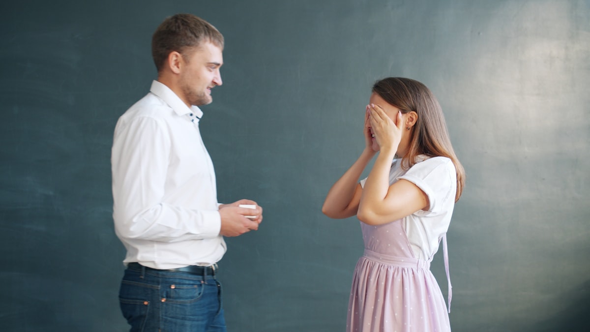 Good-looking man is proposing to pretty girl giving engagement ring in jewellery box, young lady is excited. Couple is standing against gray background. related to Bed Bug Detectives: Unmasking the Hidden Invaders