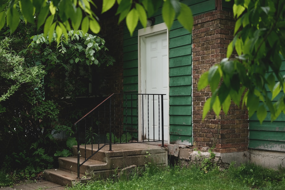 Green house with white door, concrete steps, and lush foliage. related to Step into Style: The Ultimate Guide to Entryway Shoe Trays