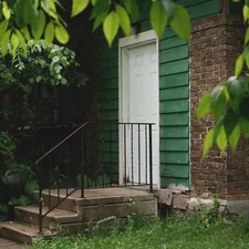 Green house with white door, concrete steps, and lush foliage. related to Step into Style: The Ultimate Guide to Entryway Shoe Trays