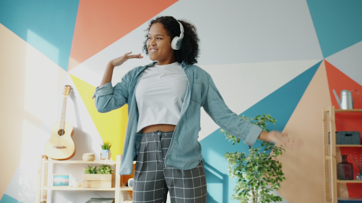 Happy Afro-American student wearing headphones is having fun at home dancing enjoying music indoors relaxing chilling. People and lifestyle concept. related to Transform Your Space: Discovering Curtains at Bed Bath and Beyond