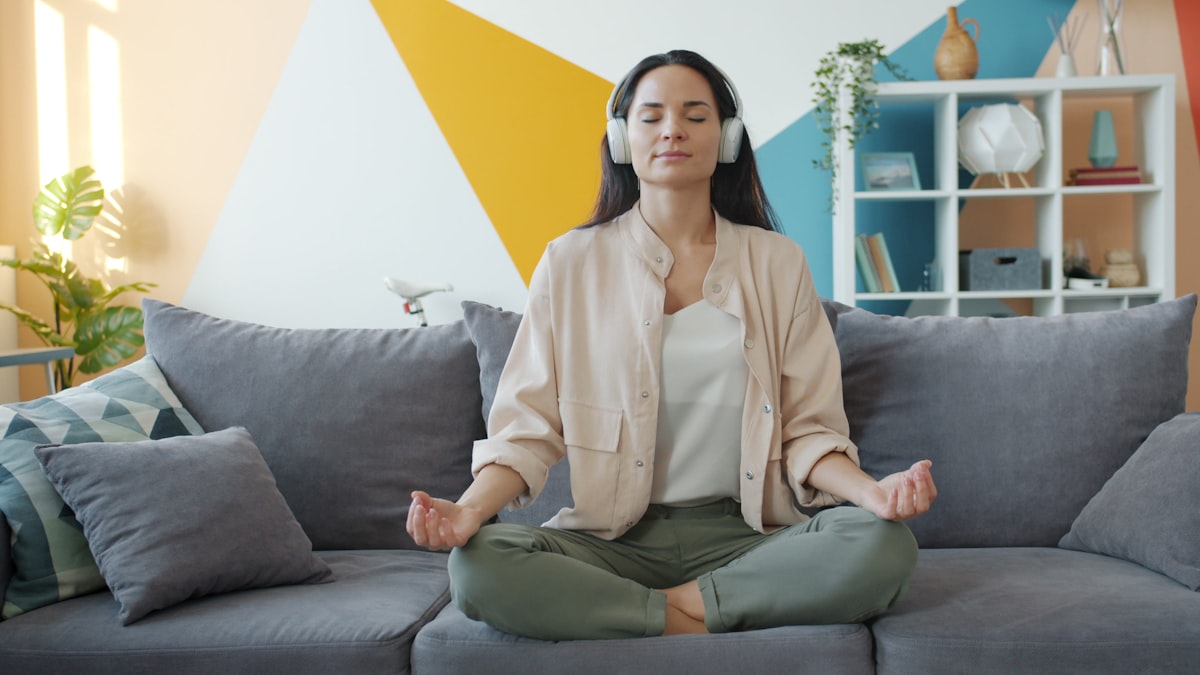 happy girl in headphones listening to music and relaxing lotus position sitting on sofa in apartment enjoying leisure time and modern technology. related to Enhancing Personal Space and Comfort with Bed Tents