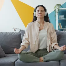 happy girl in headphones listening to music and relaxing lotus position sitting on sofa in apartment enjoying leisure time and modern technology. related to Enhancing Personal Space and Comfort with Bed Tents