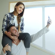Happy young couple having fun and talking online video call in the kitchen. Girl is sitting on boyfriend's neck while he holding smartphone related to Elevate Your Home's First Impression with Walmart Entryway Furniture