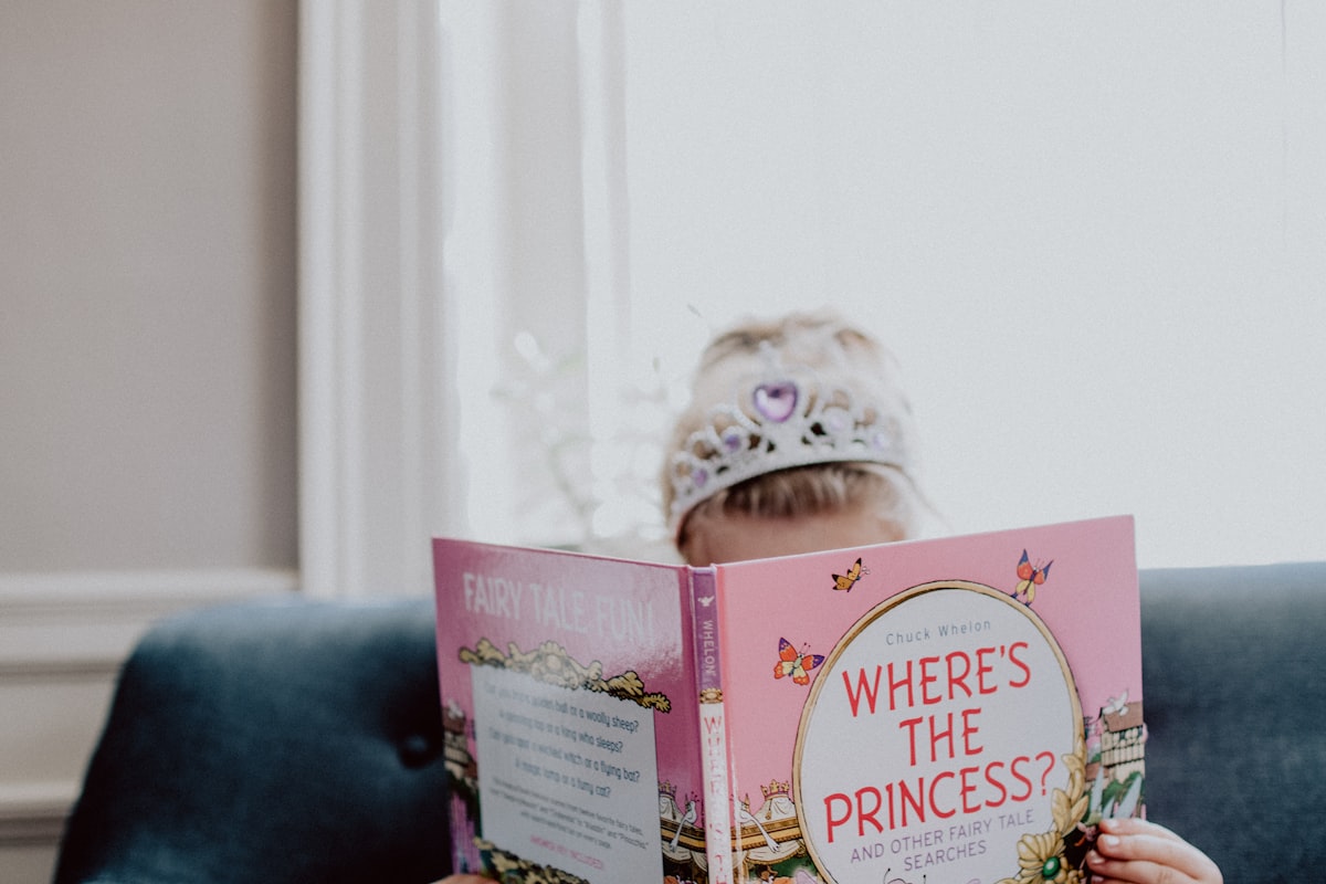 Little girl wearing a princess crown reading a "Where's the Princess" book related to Finding the Perfect Princess Crib Bedding Set for Your Little Royal
