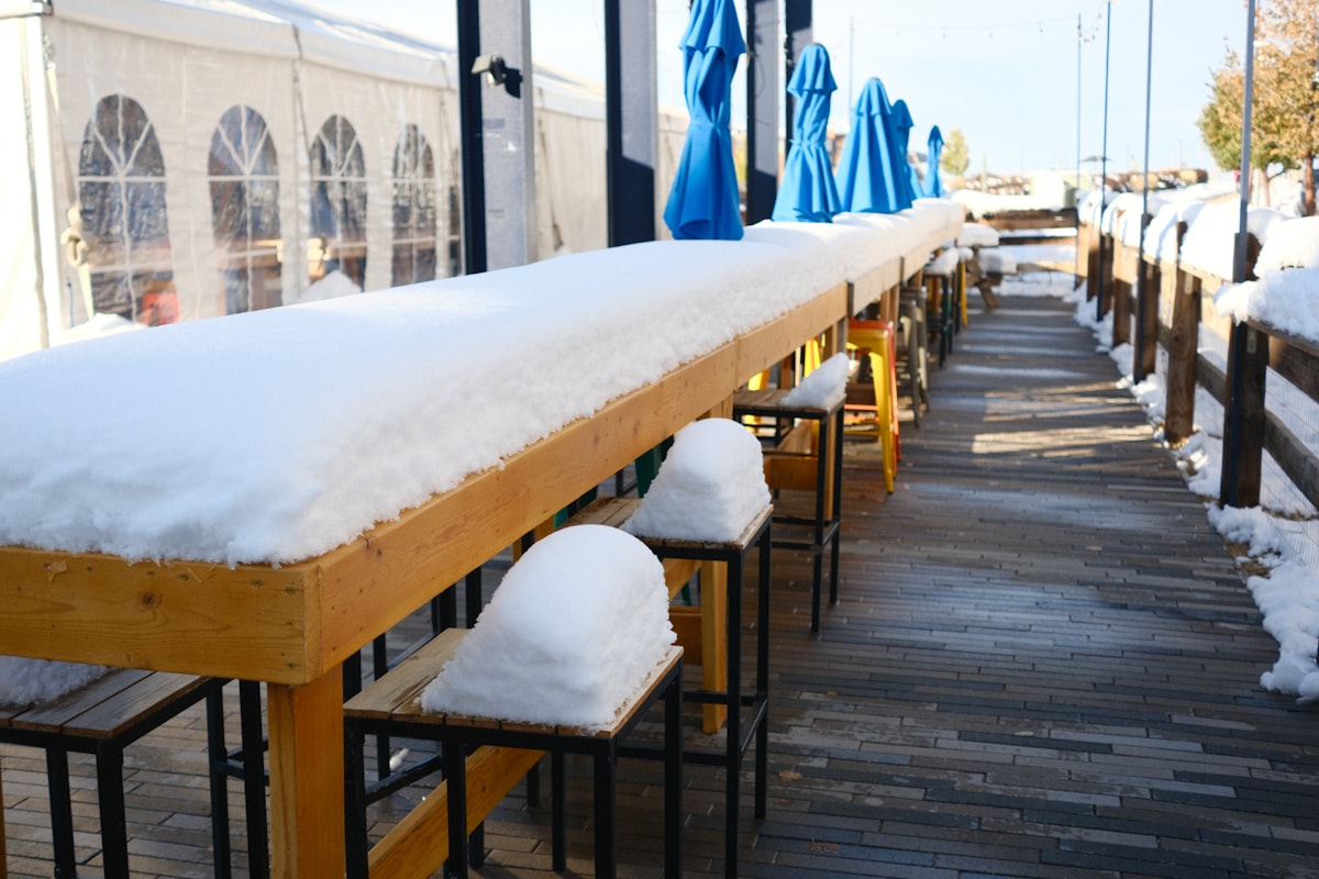 Long outdoor bar covered in snow with blue umbrellas. related to Warm Up Your Outdoor Space with a Chiminea Fireplace
