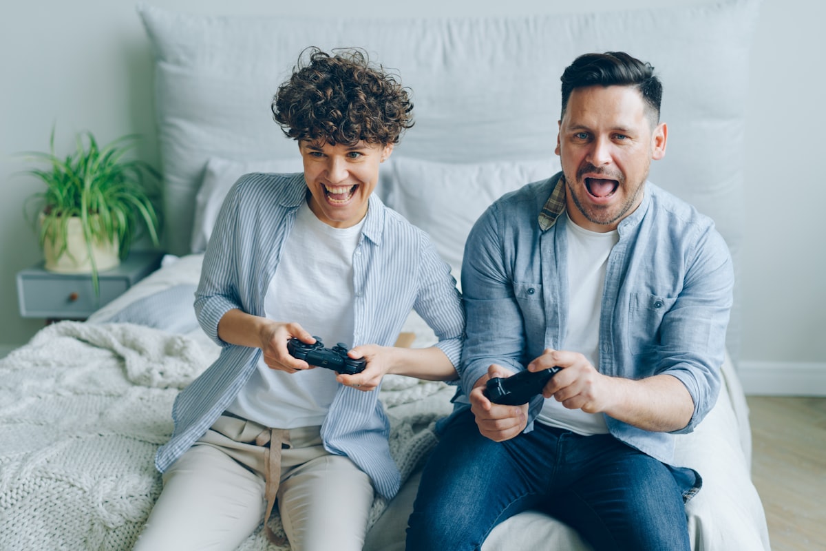 Man and woman playing video game sitting on bed in apartment having fun related to Transform Your Gaming Space: The Ultimate Guide to Gaming Bed Sheets