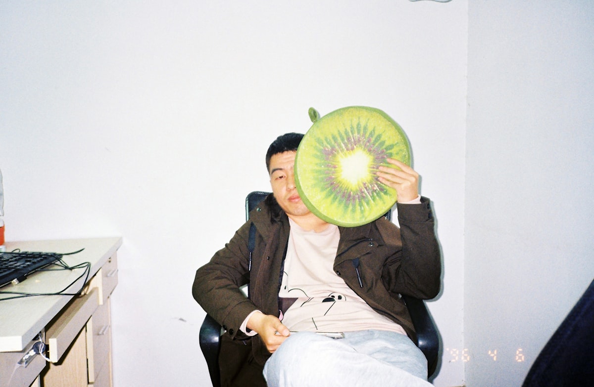 Man holding a kiwi fruit pillow in front of face related to Enhancing Comfort for Sitting in Bed