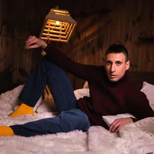 man in black sweater and blue denim jeans sitting on white fur textile related to Exploring the Lives of Jewish Men at Home