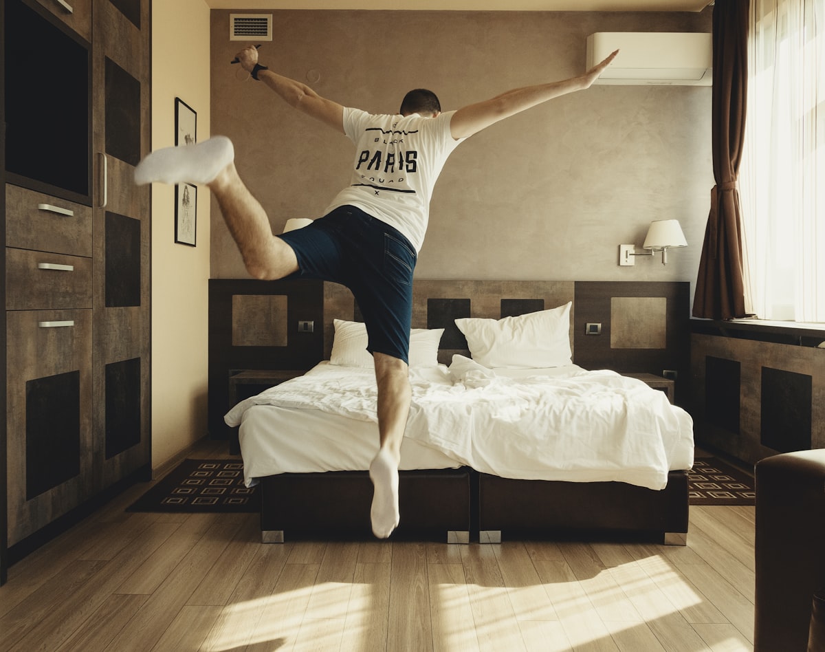 man wearing white shirt about to jump on bed related to Stylish Bedding Ideas for Teen Boys