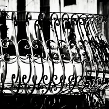 Ornate wrought iron balcony railing with scrollwork details, captured in high contrast black and white. The intricate curves and spirals reflect the craftsmanship of colonial-era architecture. related to Wrought Iron Bed Frames - Elevate Your Home's Style