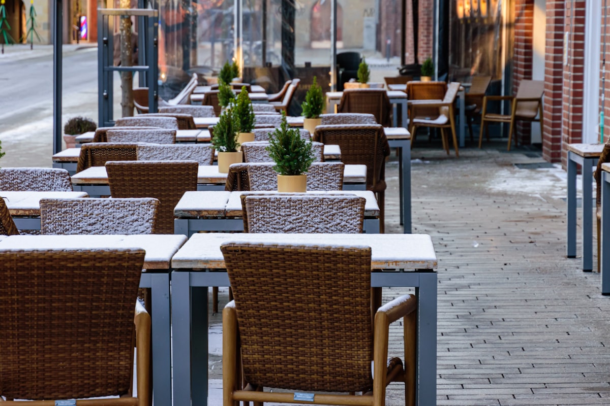 Outdoor cafe tables and chairs covered in light snow. related to Warm Up Your Outdoor Space with a Chiminea: Where to Find the Perfect One
