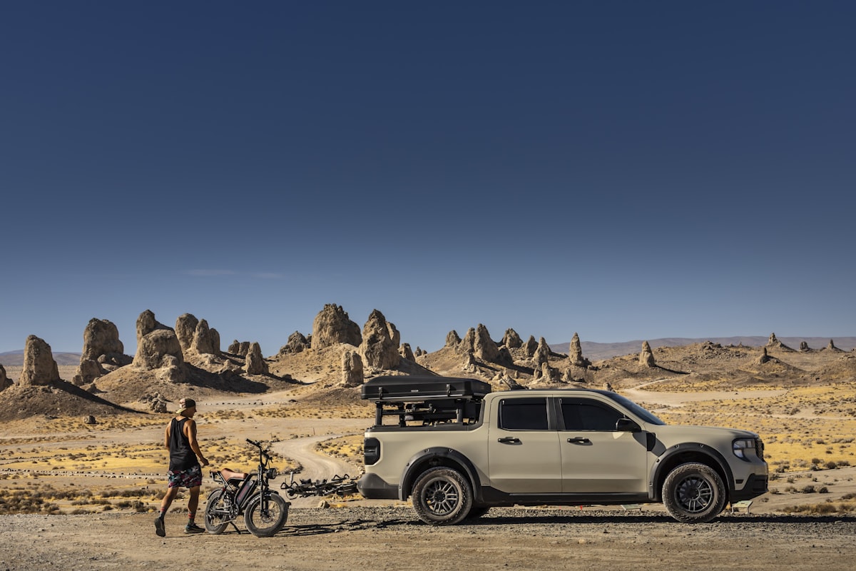 Person and bike beside truck, desert landscape with rock towers. related to Essential Accessories for Overlanding and Adventure Vehicles