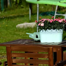 Pink flowers, watering can on wooden outdoor table. related to Transform Your Outdoor Space with Lowe's Cast Iron Chimineas