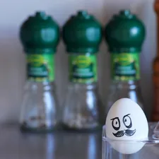 President Lukashenko's evil face painted on a white egg. Painted face on a pure white egg in a stand, lying in the kitchen against the background of spices and blurred wall. Political caricature in the kitchen related to Cozy Up with the Green Egg Chiminea