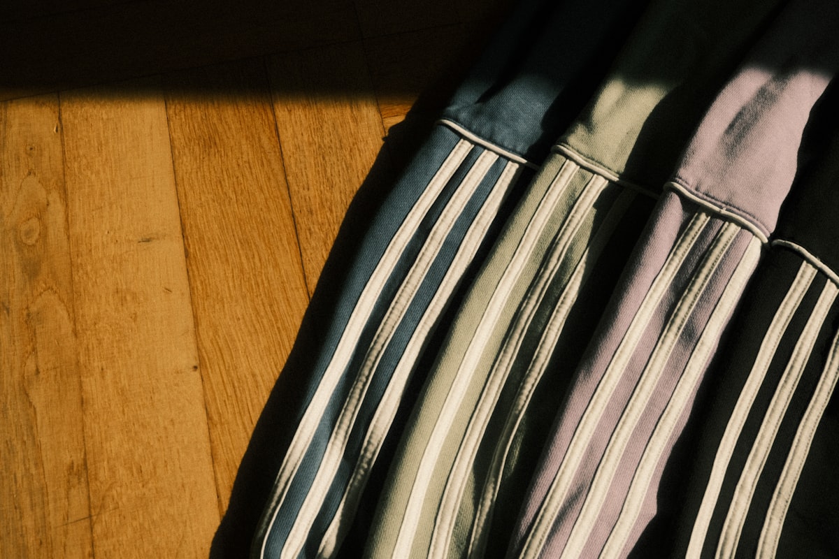 Row of colorful Adidas hoodies in blue, black, pink and green draped on wooden floor, soft sunlight shadows. related to Transform Your Bedroom with a Striped Bed Skirt
