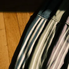 Row of colorful Adidas hoodies in blue, black, pink and green draped on wooden floor, soft sunlight shadows. related to Transform Your Bedroom with a Striped Bed Skirt