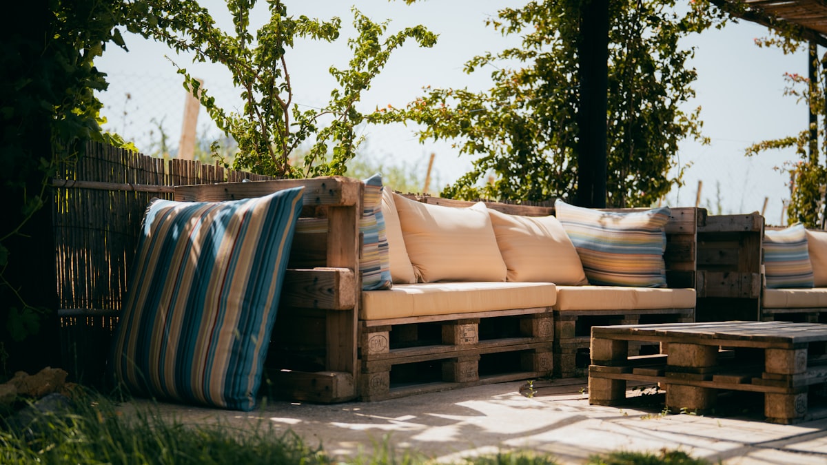 Rustic outdoor patio with pallet sofa and cushions under trees. related to How to Make a Pallet Bed: 5 Creative Ideas