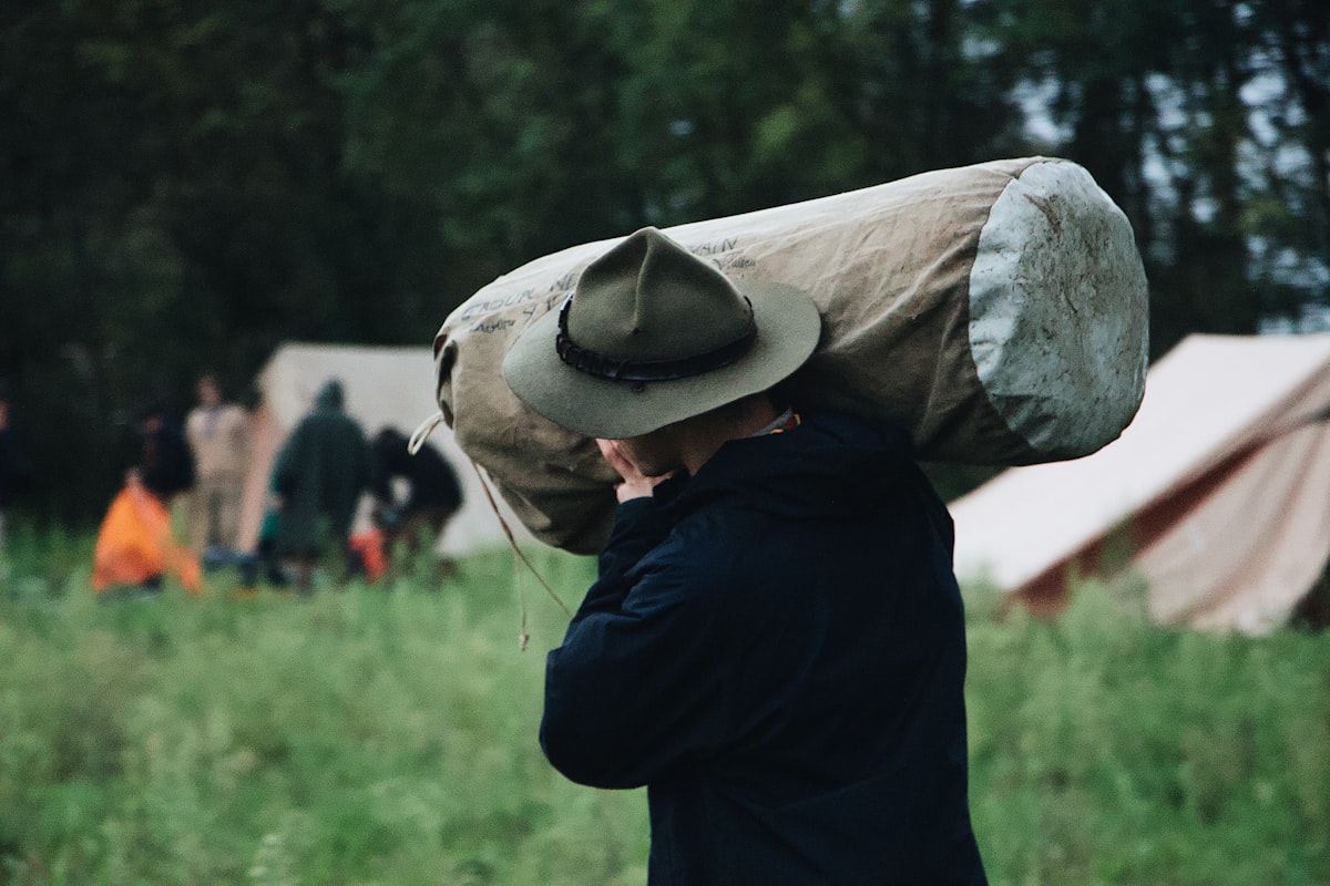 selective focus photography of walking man carrying bag near set-up tent related to The Ultimate Guide to Canvas Bed Rolls