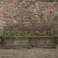 Stone planter with flowers placed against an old brick wall. Rustic urban detail, gardening, textures, outdoor decor, European courtyard aesthetic. related to Unlocking the Potential of Raised Flower Bed Kits