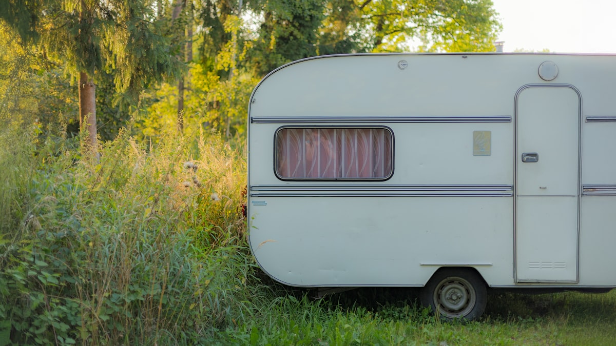 This image captures a vintage caravan resting peacefully in a lush, green woodland clearing. The soft afternoon light filters through the trees, casting a warm glow on the weathered exterior of the camper. The scene evokes a sense of quiet adventure and nostalgic tranquility, perfect for themes of travel, escape, and the simple beauty of nature. related to Cozy Up on the Open Road: The Ultimate Guide to Travel Trailer Bedding