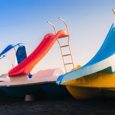 Three colorful pedal boats with slides under a clear sky. related to Unleashing Slumber Fun for Kids: The World of Beds with Slides