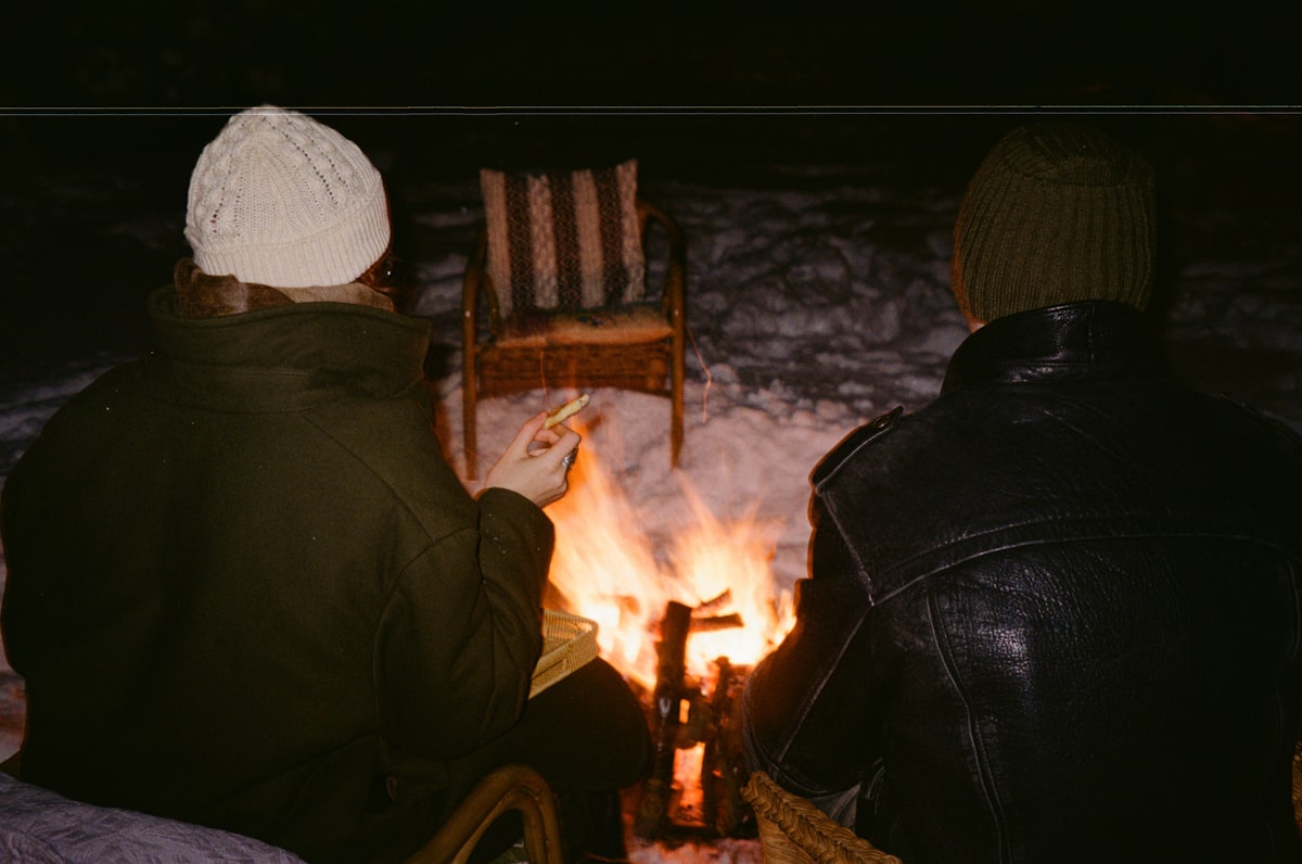 Two people sit by a campfire at night. related to Camping Beds for a Cozy Night Under the Stars: Walmart Options