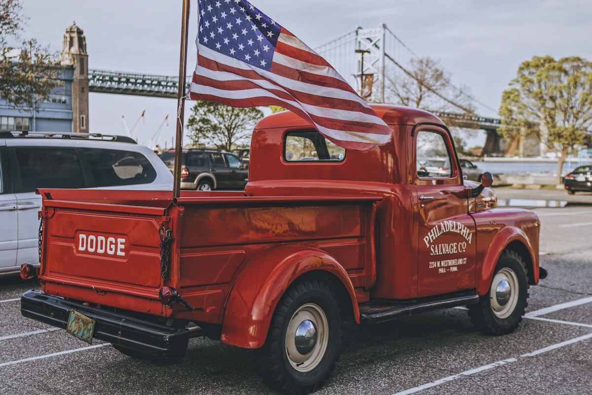 Vintage cherry red Dodge pickup truck parked at Penn's Landing, with a view of the Benjamin Franklin Bridge in Old City, Philadelphia, PA. related to The Ultimate Guide to Flag Pole Mounts for Truck Beds