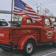 Vintage cherry red Dodge pickup truck parked at Penn's Landing, with a view of the Benjamin Franklin Bridge in Old City, Philadelphia, PA. related to The Ultimate Guide to Flag Pole Mounts for Truck Beds