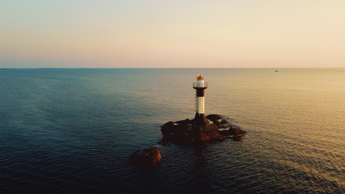 white and red lighthouse on rock formation near body of water during daytime related to Beacon of Comfort: Lighthouse Bed and Breakfast Getaways