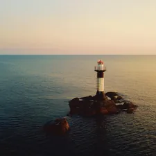 white and red lighthouse on rock formation near body of water during daytime related to Beacon of Comfort: Lighthouse Bed and Breakfast Getaways