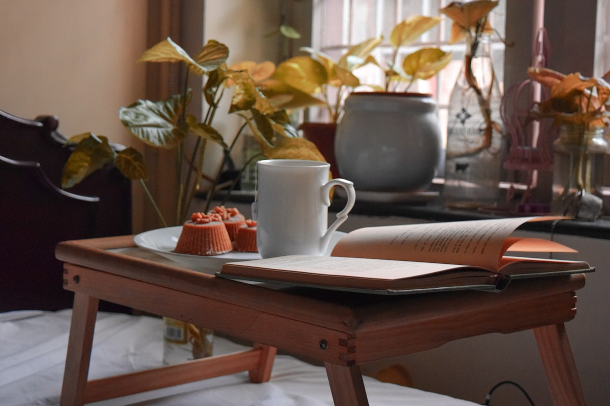 white ceramic mug on white book page on brown wooden table related to Elevating Your Comfort: The Adjustable Bed Table Solution