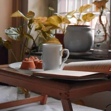 white ceramic mug on white book page on brown wooden table related to Elevating Your Comfort: The Adjustable Bed Table Solution