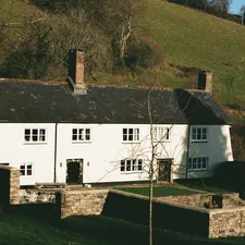 White farmhouse with stone walls and green hills. related to Discover the Charm of Bed and Breakfast Hill Country
