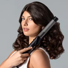 With a confident gaze, a woman uses a TYMO curling iron to perfect her bouncy curls, capturing the essence of modern elegance in hair styling. related to Achieve Salon-Quality Styles at Home with the Bed Head Flat Iron