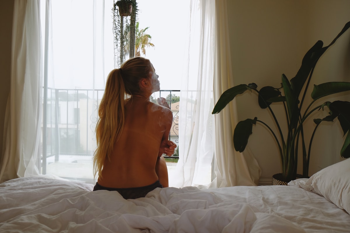 woman in orange tank top and black skirt sitting on bed related to Brighten Up Your Bedroom with a Hot Pink Coverlet