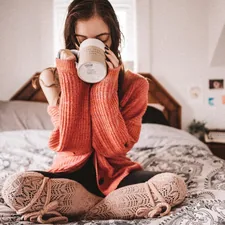 woman in red knit sweater holding white ceramic mug related to Power Up for Sleep: The Benefits of Drinking Milk Before Bed