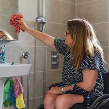 Woman in wheelchair cleaning bathroom mirror related to Finding Comfort and Safety in the Shower: A Guide to Shower Chairs at Bed Bath and Beyond