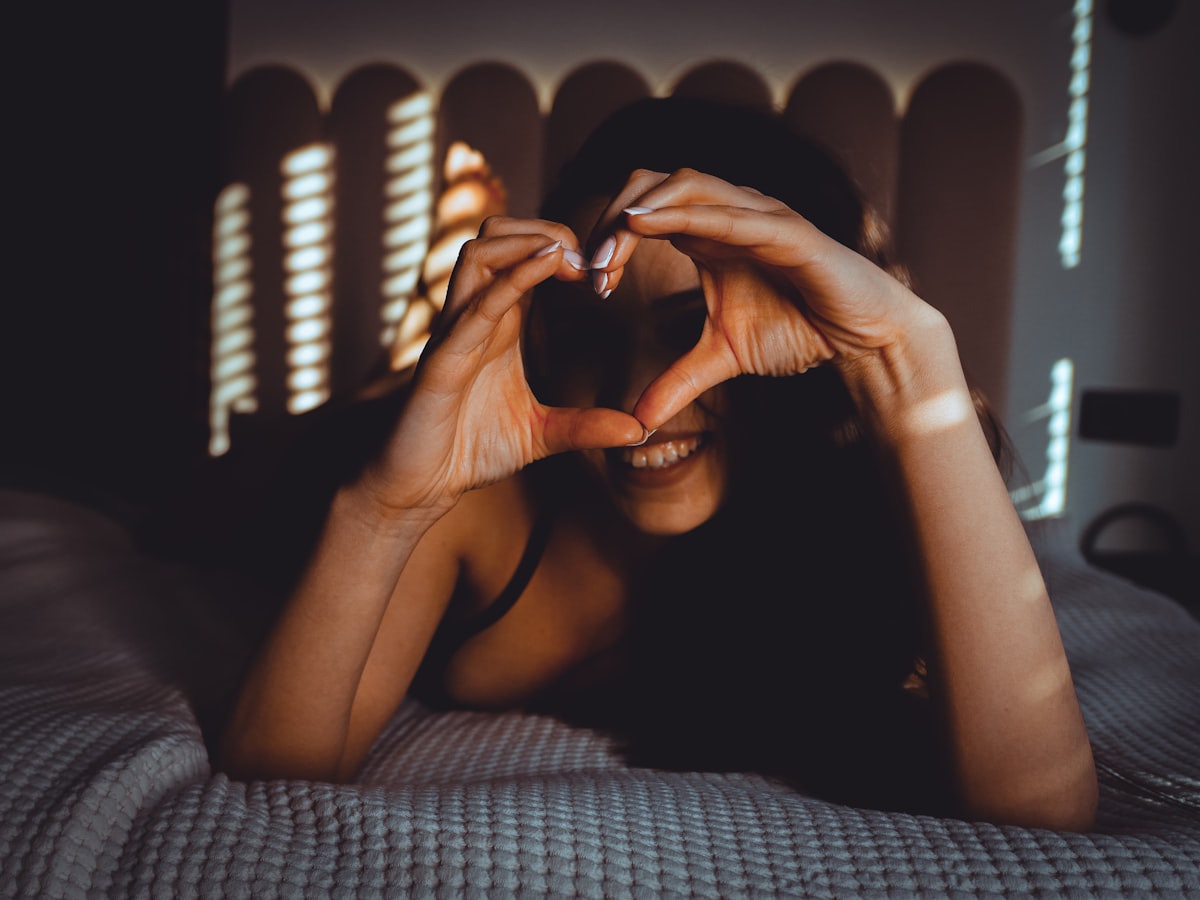 Woman makes heart shape with hands on bed related to A Heart Shaped Bed: The Ultimate Symbol of Romance
