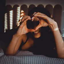Woman makes heart shape with hands on bed related to A Heart Shaped Bed: The Ultimate Symbol of Romance