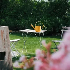 Yellow watering can on a small table in a garden. related to Transform Your Outdoor Space with a Wood Burning Chiminea: A Comprehensive Guide