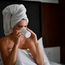 Young blonde woman with a white towel wrapped around her head drinking hot coffee in bed during her morning routine. related to Sleep Better with Bed Head Products: Expert Reviews and Buying Guide