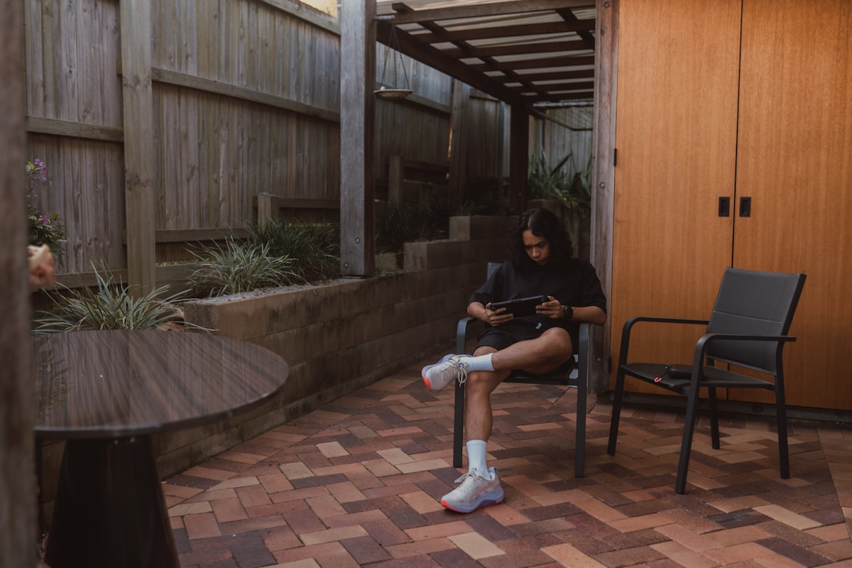 Young woman on patio using tablet in a fenced yard. related to Protect Your Outdoor Living Space with Chiminea Decking Protectors
